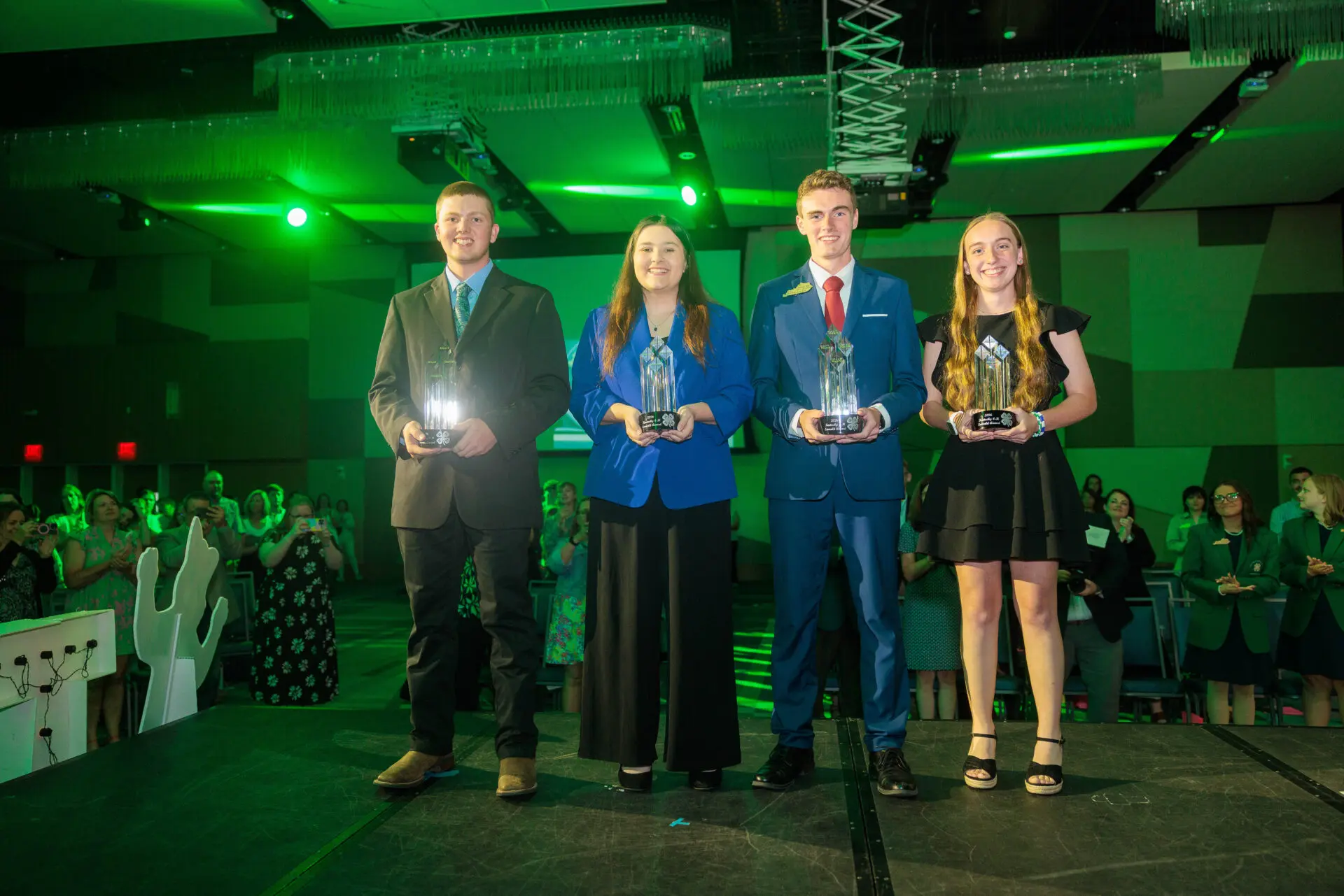 Four Emerald Winners on the Stage at Teen Conference holding their large crystal trophy